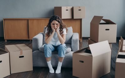 Unhappy young woman sitting in empty room near cardboard boxes feel unmotivated to pack her belongings. Spanish girl is sad because of relocation. Hard moving day, divorce concept.